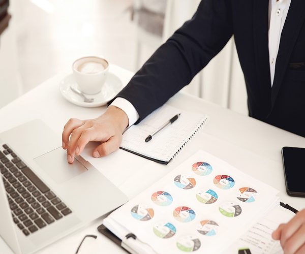 Cropped frontview of a businessman working place at the restaurant with laptop, cellphone, diagrams and latte